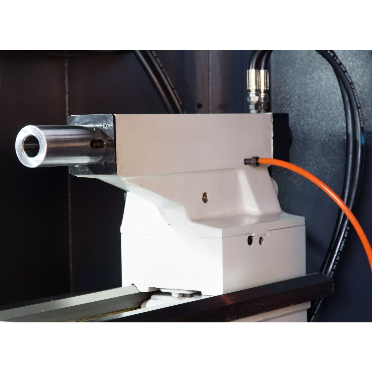 Detailansicht einer CNC-Drehmaschine mit Reitstockeinheit, Hydraulikleitungen und orangefarbener Anschlussleitung.