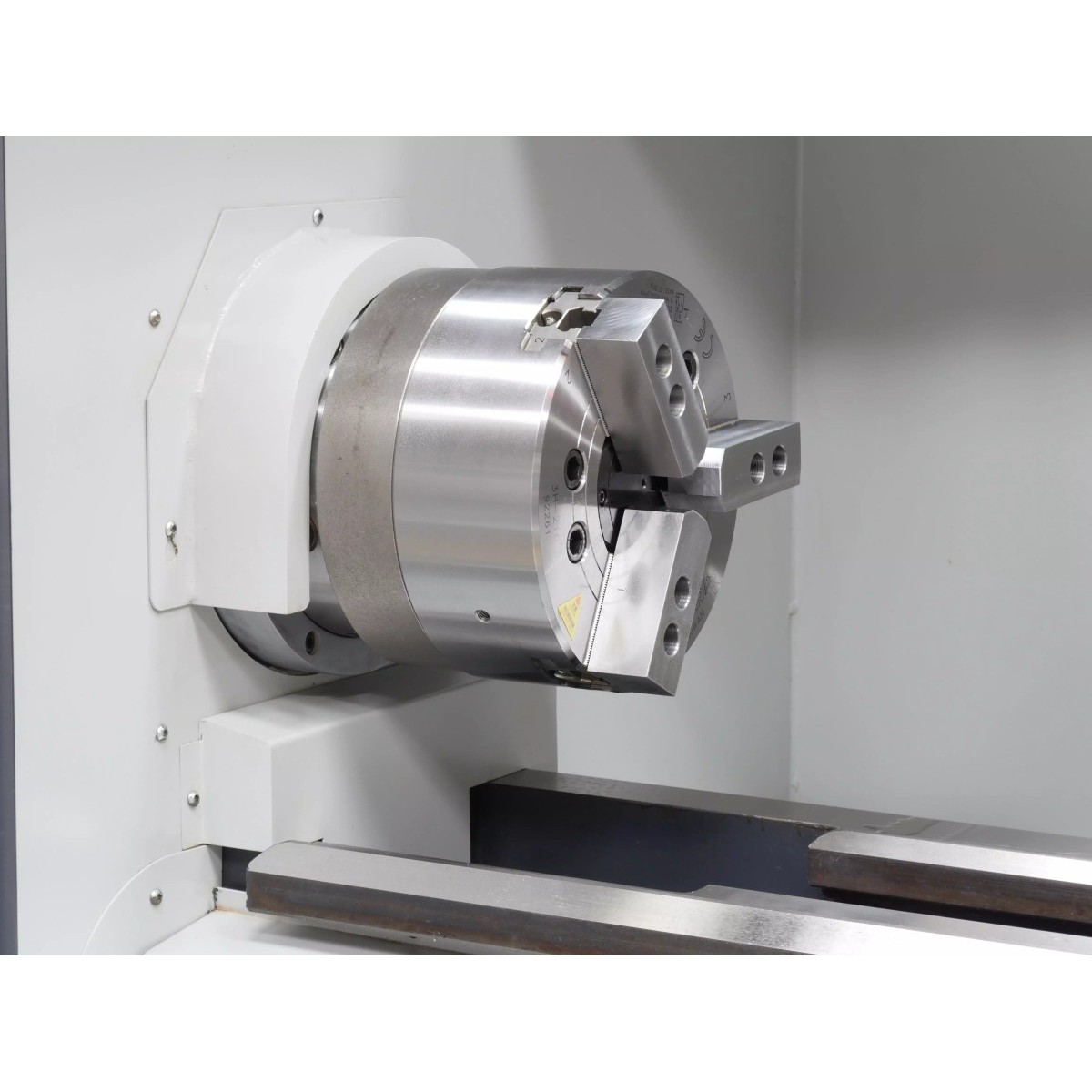 Detailansicht einer CNC-Drehmaschine mit Reitstockeinheit, Hydraulikleitungen und orangefarbener Anschlussleitung.