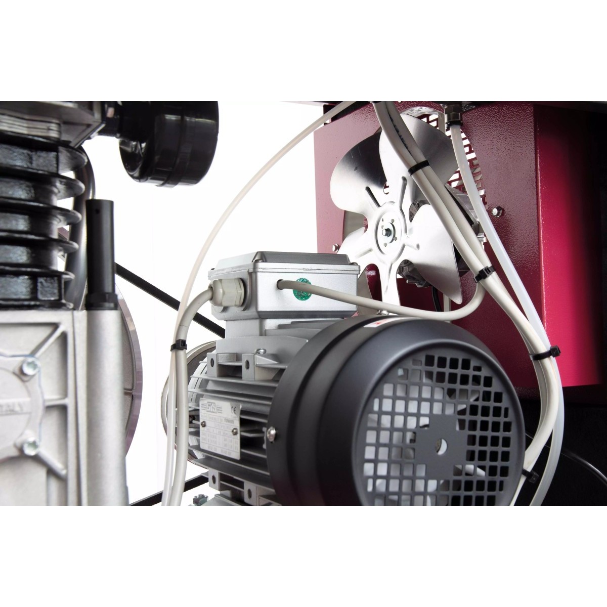 Nahaufnahme eines Kompressors: Elektromotor mit Lüftergitter, Kabel und Gehäuse; dahinter sichtbarer Ventilator in rotem Rahmen.