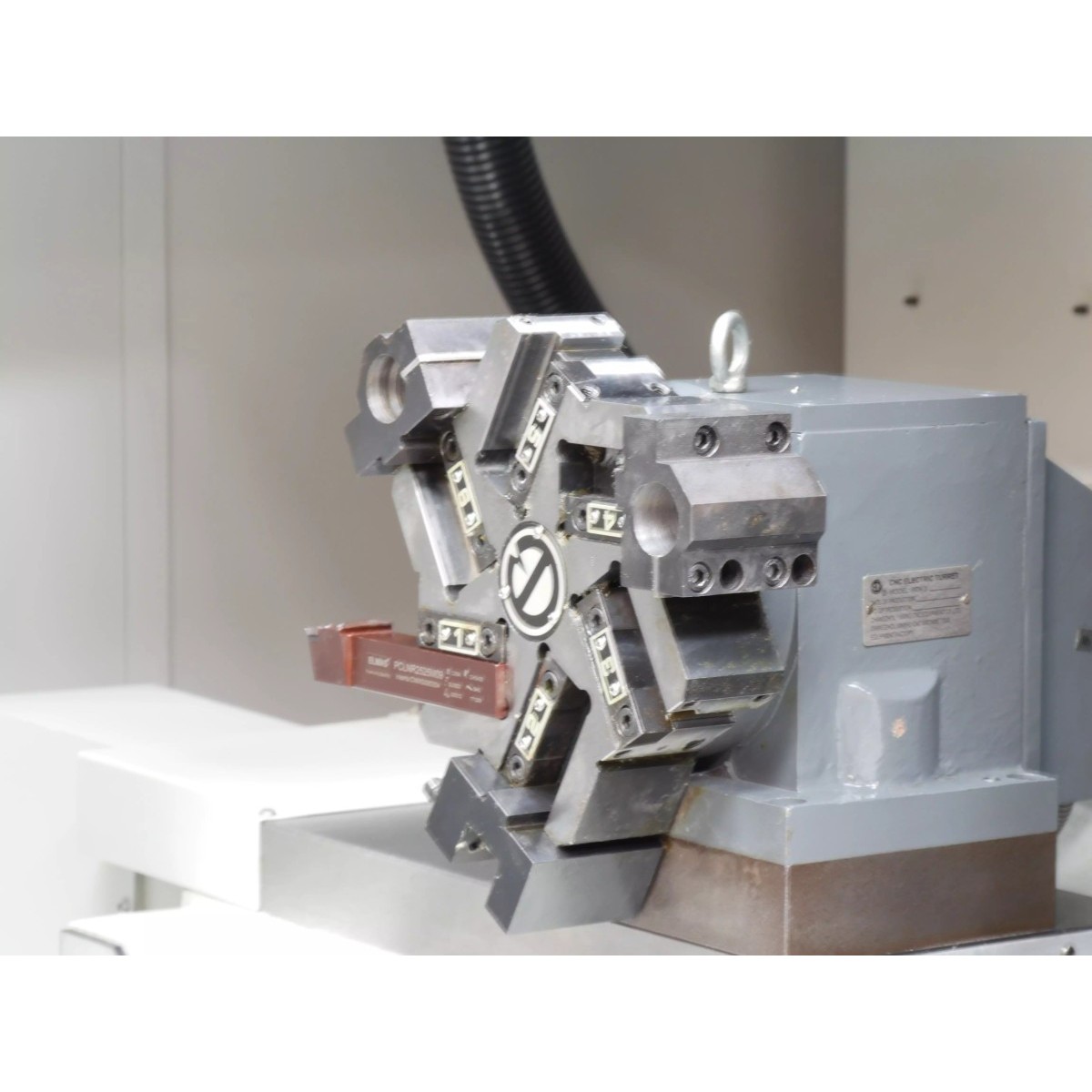 Detailansicht einer CNC-Drehmaschine mit Reitstockeinheit, Hydraulikleitungen und orangefarbener Anschlussleitung.