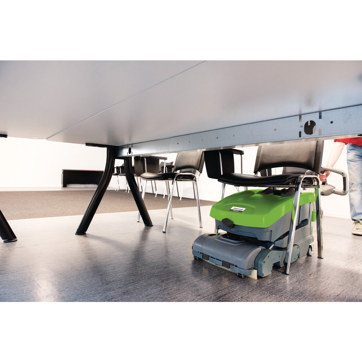 Reinigungsmaschine im Einsatz unter einem Tisch, reinigt den Boden zwischen Stuhlbeinen.
