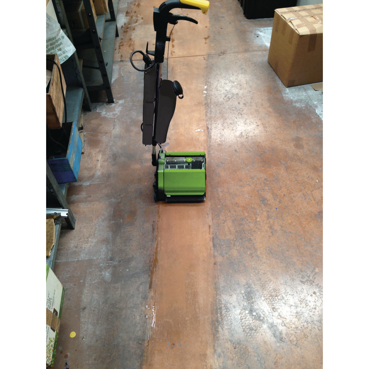 Bodenreinigungsmaschine säubert schmalen Gang mit sichtbarem Reinigungsergebnis.