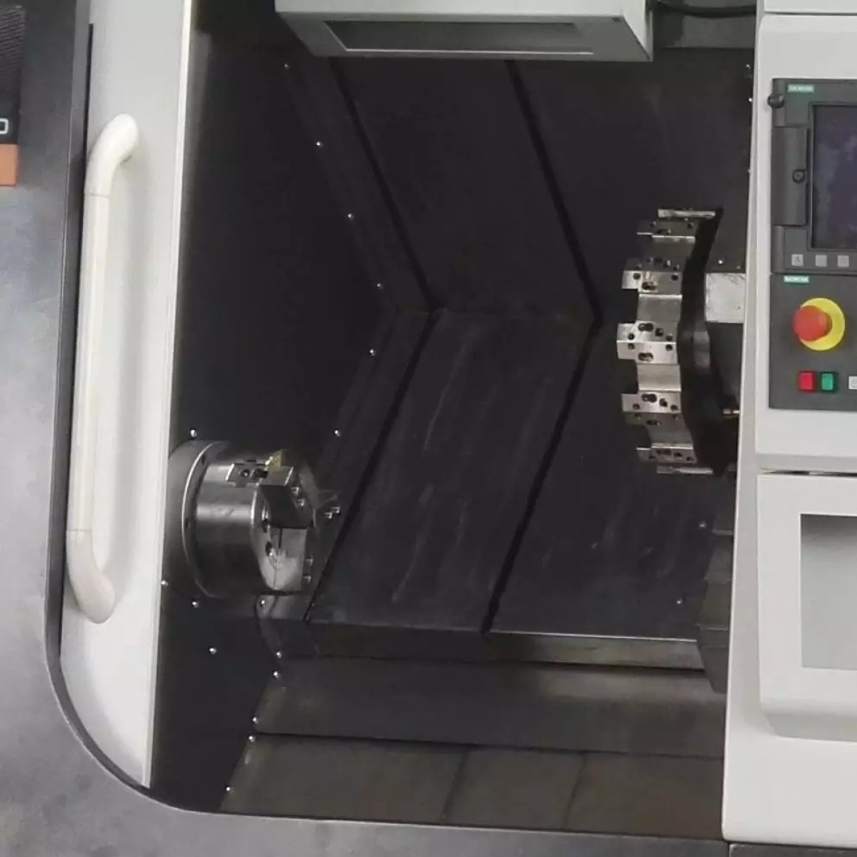 Innenansicht einer CNC-Drehmaschine mit Dreibackenfutter, Werkzeugrevolver und teilweise sichtbarem Bedienfeld.