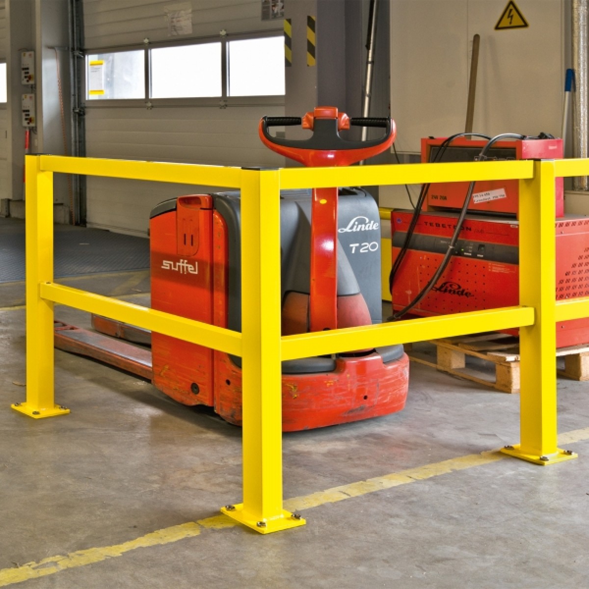 BLACK BULL Rammschutz-Geländer S-Line - Querbalken Gelbes Schutzgeländer vor einem roten Elektro-Hubwagen und roten Ladegeräten in einer Halle.
